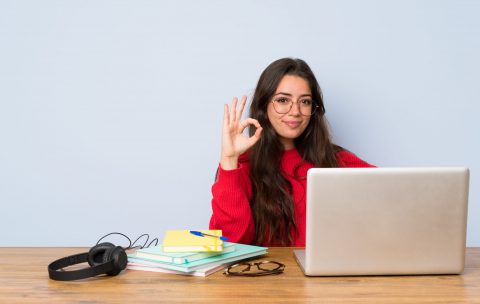 Teenager student girl studying in a table showing ok sign with fingers