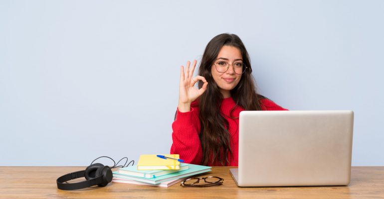 Teenager student girl studying in a table showing ok sign with fingers